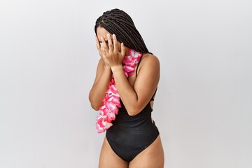 Young african american woman wearing swimsuit and hawaiian lei with sad expression covering face...