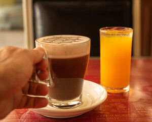Close up a hand holding a cup of coffee. A glass of orange juice  on the table on the background
