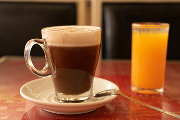 Close up a cup of coffee on the table. A glass of orange juice on the background