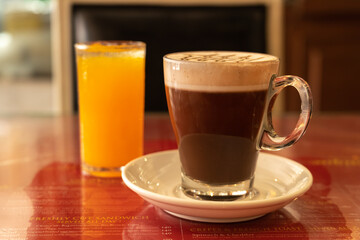 Close up a cup of coffee on the table. A glass of orange juice on the background