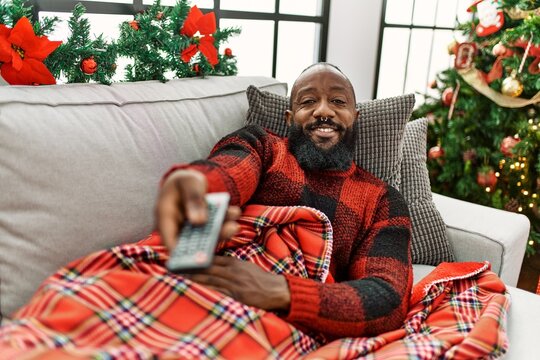 Young African American Man Watching Tv Lying By Christmas Tree At Home