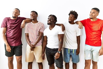 Young african group of friends standing together over isolated background looking away to side with smile on face, natural expression. laughing confident.