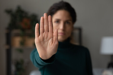 Stop it. Strong serious young lady extending hand forward forbidding saying no to harassment bullying abuse violence against women. Focus on female palm demonstrating gesture of rejection prohibition