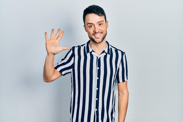 Fototapeta premium Young hispanic man wearing casual clothes showing and pointing up with fingers number five while smiling confident and happy.
