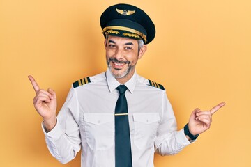 Handsome middle age man with grey hair wearing airplane pilot uniform smiling confident pointing with fingers to different directions. copy space for advertisement