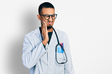 Young african american man wearing doctor uniform and stethoscope touching mouth with hand with painful expression because of toothache or dental illness on teeth. dentist