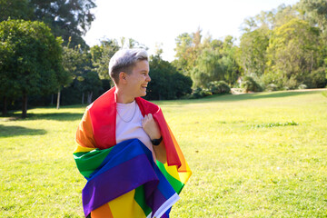 gender non-binary person is rolled up with the gay pride flag on his body. She is looking at the camera. Concept of non-binary and androgynous. Diversity and gay pride.