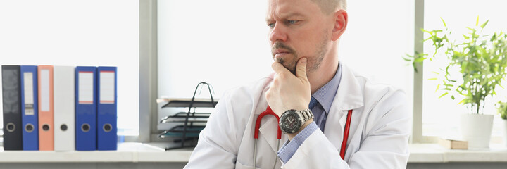 Pensive doctor looking at laptop screen and typing on keyboard in clinic