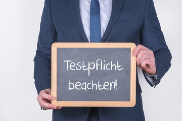 Geschäftsführer oder Chef mit einer Tafel auf der Testpflicht beachten steht