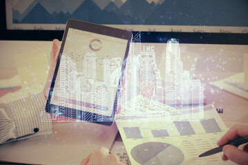 Double exposure of man's hands holding and using a digital device and city drawing.