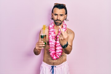 Young hispanic man wearing swimsuit and hawaiian lei drinking tropical cocktail showing middle...