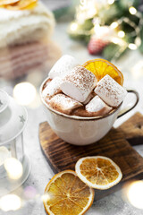 Traditional Christmas cocoa in a ceramic cup with marshmallows and orange chips on a light background with bokeh	