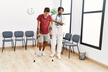Two men physiptherapist and patient having medical consultation walking using crutches at hospital waiting room