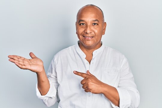 Middle age latin man wearing casual clothes amazed and smiling to the camera while presenting with hand and pointing with finger.