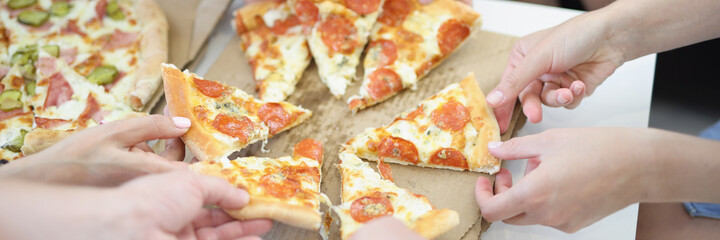 Lots of adults and childrens hands taking slices of delicious appetizing pizza closeup