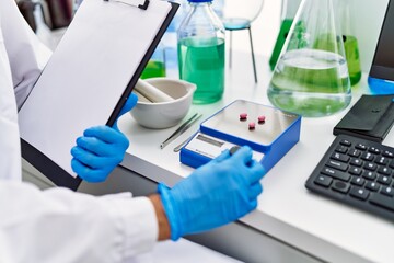 Young hispanic man wearing scientist uniform weighing pills at laboratory