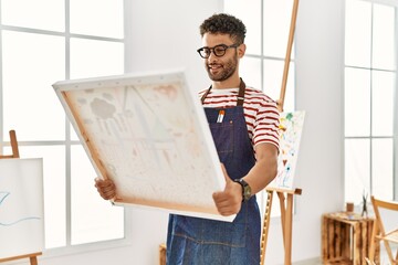 Young arab artist man smiling happy holding canvas at art studio.