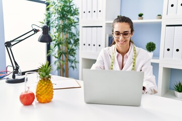 Young hispanic woman working at dietitian clinic looking positive and happy standing and smiling...