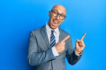 Bald man with beard wearing business jacket and glasses smiling and looking at the camera pointing with two hands and fingers to the side.