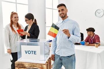 Young belgian voter man smiling happy holding belgium flag at vote center.