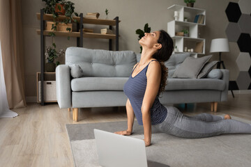 Strengthening muscles. Fit young hispanic woman do yoga exercises on floor before computer screen....