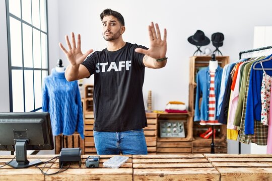 Young hispanic man working at retail boutique doing stop gesture with hands palms, angry and frustration expression