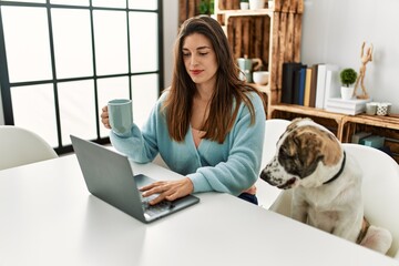 Young woman using laptop sitting on table with dog at home