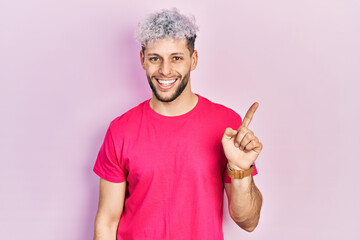 Young hispanic man with modern dyed hair wearing casual pink t shirt with a big smile on face, pointing with hand finger to the side looking at the camera.