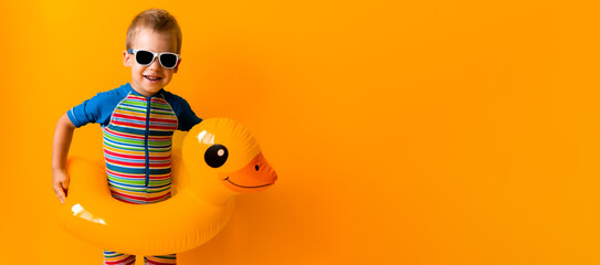 banner happy little smiling child swimmer sport boy wear sun glasses swimsuit, Kid Inflatable swimming ring yellow duck point to side away, isolated orange background. hot summer vacation copy space