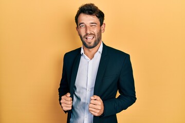 Handsome man with beard wearing business suit holding jacket winking looking at the camera with...