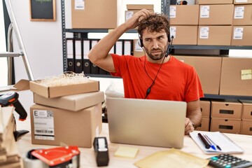 Young hispanic call center agent man working at warehouse confuse and wondering about question. uncertain with doubt, thinking with hand on head. pensive concept.