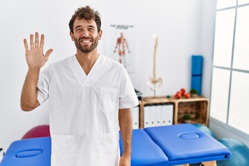 Young handsome physiotherapist man working at pain recovery clinic showing and pointing up with...