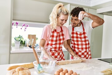 Young couple smiling happy kneading dough with hands at kitchen.