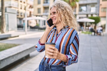 Fototapeta premium Middle age blonde woman talking on the smartphone drinking coffee at street