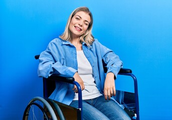 Beautiful caucasian woman sitting on wheelchair winking looking at the camera with sexy expression,...