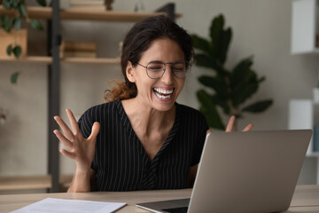 Overjoyed young casual hispanic woman employee in glasses having fun chat with colleague on laptop in corporate web conference app. Laughing millennial female worker watch funny video at social media