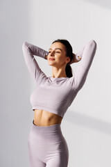 Young fit woman making ponytail posing in sportswear against white background.