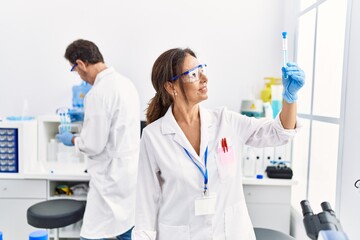 Middle age man and woman partners wearing scientist uniform holding test tube at laboratory