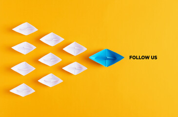 Yellow paper boat leads white paper ships with the follow us message. Social media or internet followers concept. - obrazy, fototapety, plakaty