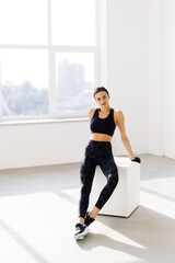 Young woman sitting on a box at gym after her workout. Female athlete taking rest after exercising at gym.