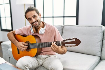 Handsome hispanic man playing guitar at the living room at home