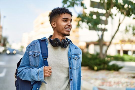 Hispanic young man smiling wearing headphones at the street