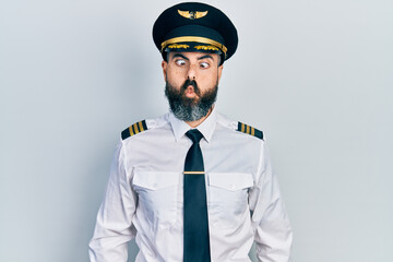 Young hispanic man wearing airplane pilot uniform making fish face with lips, crazy and comical gesture. funny expression.