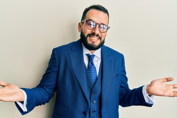 Young man with beard wearing business suit and tie clueless and confused expression with arms and...