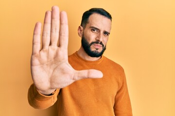 Young man with beard wearing casual winter sweater doing stop sing with palm of the hand. warning expression with negative and serious gesture on the face.