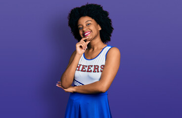 Young african american woman wearing cheerleader uniform looking confident at the camera with smile with crossed arms and hand raised on chin. thinking positive.