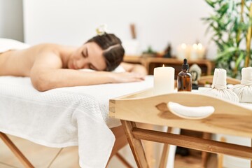 Young hispanic woman lying on massage table at beauty center.