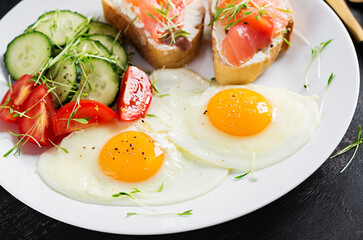 Fototapeta na wymiar Diet breakfast. Fried eggs and sandwiches with salt salmon and fresh salad.