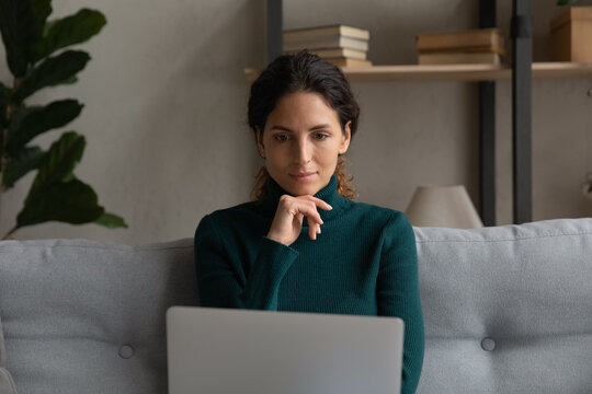 Thinking By Laptop. Thoughtful Hispanic Lady Use Laptop On Sofa At Home Ponder On Working Problem Read Information On Screen. Young Female Remote Worker Hold Pc Consider On Electronic Document