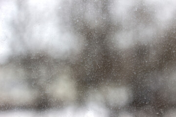 Dusty glass covered with dried rain drops. Snow falling outside the window on a cold winter day.